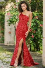 A woman poses confidently in a sparkling red dress with a thigh-high slit, surrounded by lush greenery and weathered stone walls, creating an elegant and vibrant outdoor setting.