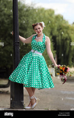 Woman in vintage polka dot dress leaning from a lamp post holding a bunch of flowers Stock Photo