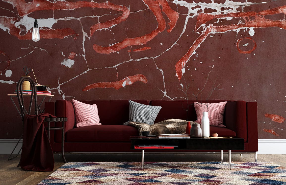 Rustic red abstract cracked earth mural wallpaper behind maroon sofa with geometric rug in living room.