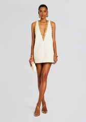 White beaded mini dress with gold sequin trim and deep V neckline, styled with gold jewelry and strappy sandals.