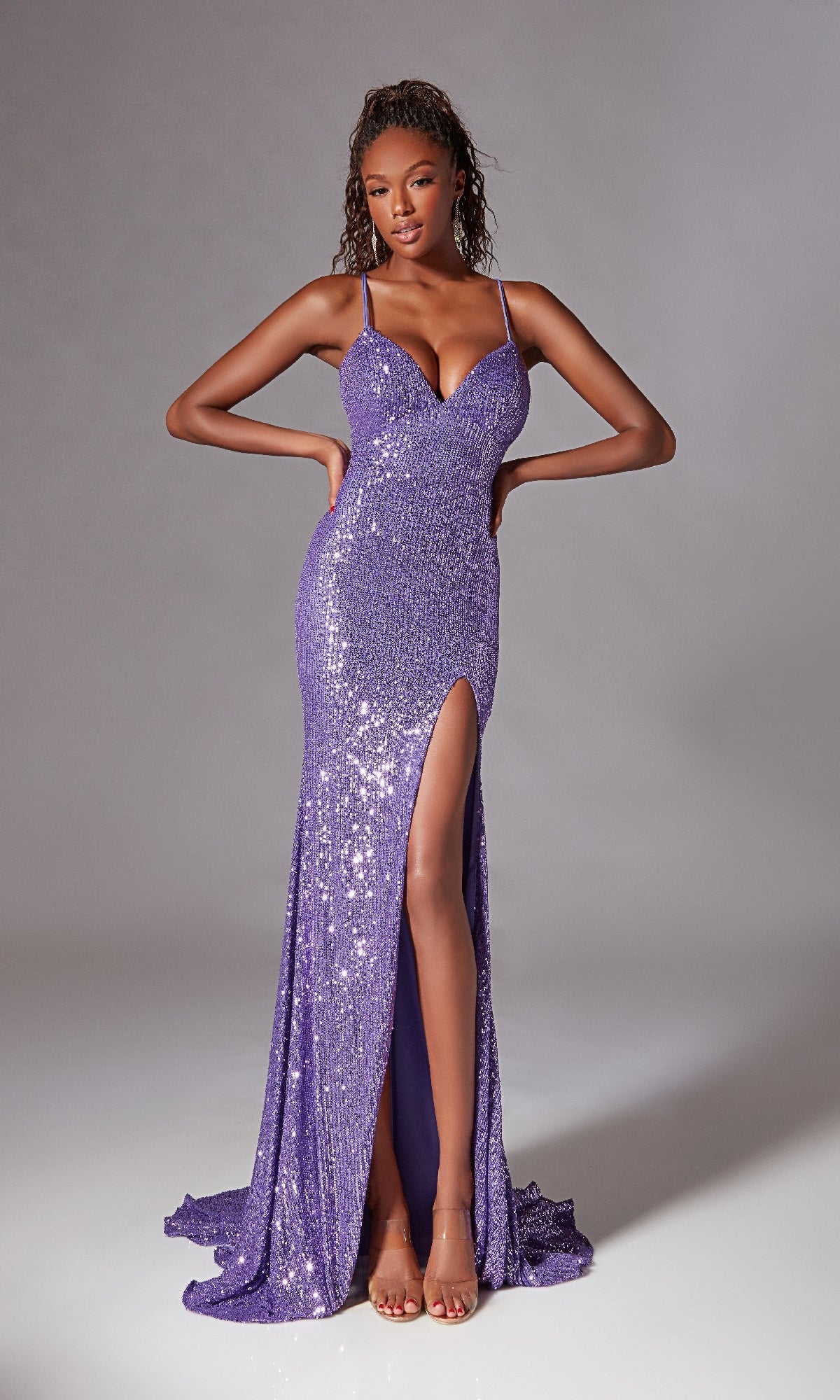 A woman models the Strappy Long Sequin Prom Dress: Aerie Couture 261, featuring a strappy back, purple sequins, thigh-high slit, and open-toe heels against a plain gray background.