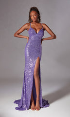 A woman models the Strappy Long Sequin Prom Dress: Aerie Couture 261, featuring a strappy back, purple sequins, thigh-high slit, and open-toe heels against a plain gray background.