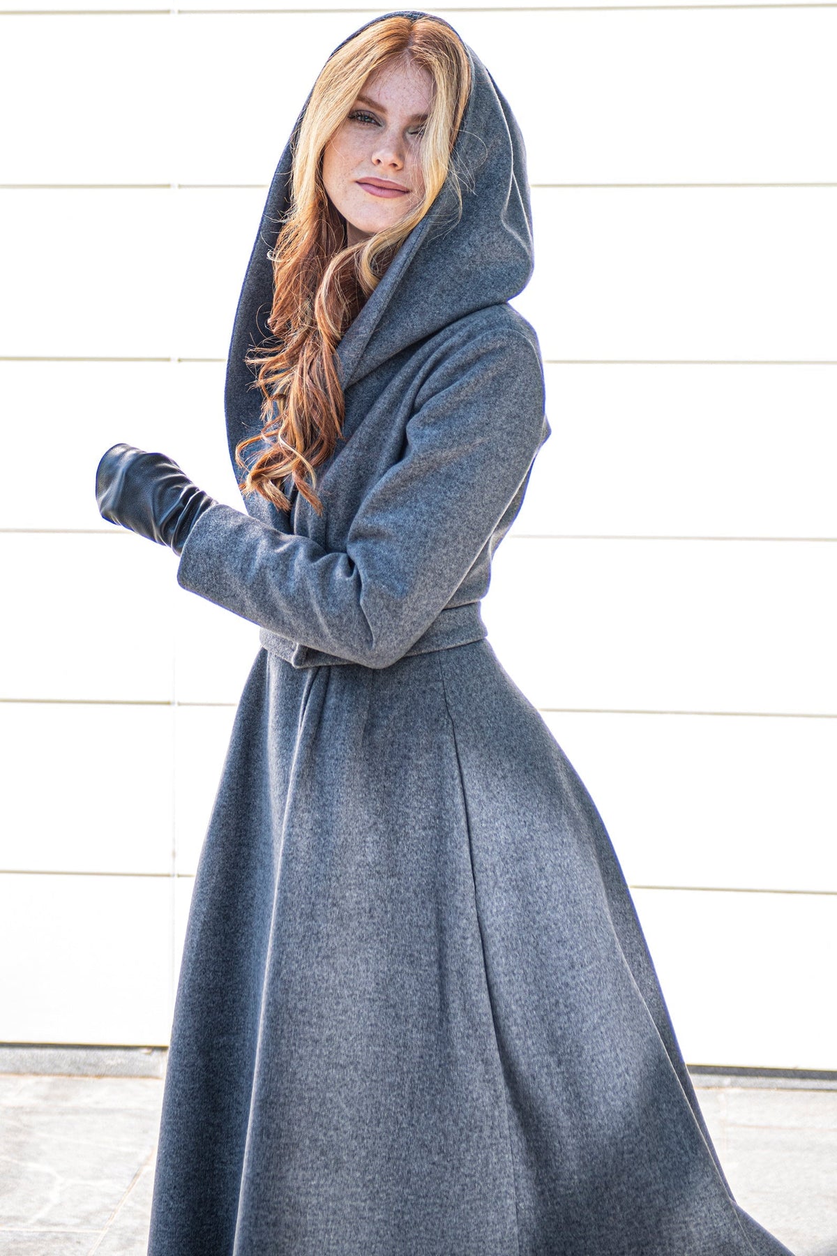 Woman wearing a gray Princess Winter Coat with a tie waist and slouchy hood standing outdoors