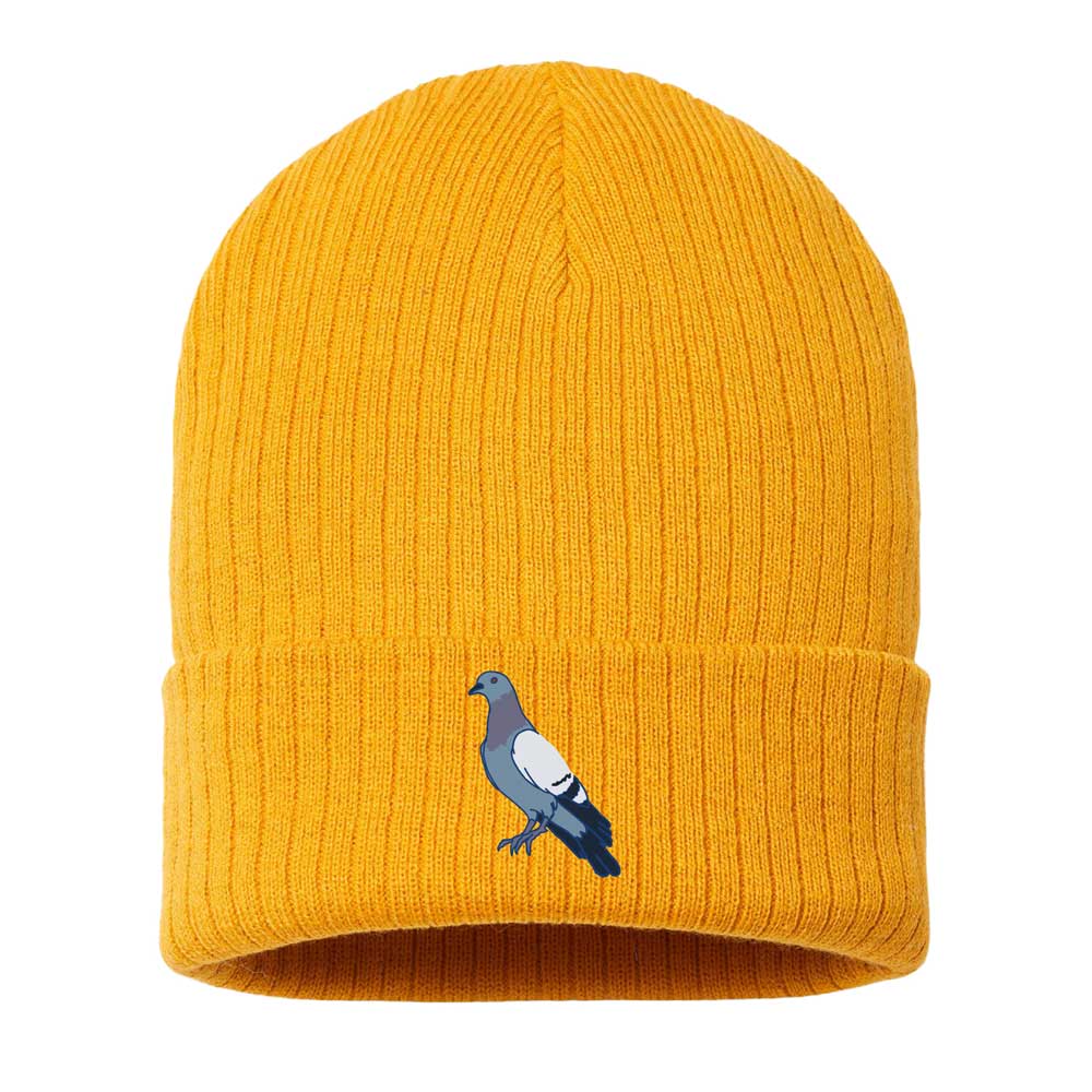 The Roberto Lugo Pigeon Beanie is a bright yellow, ribbed knit hat with a folded brim and an embroidered pigeon graphic on the front, inspired by artful heritage and featured at The Henry Ford Museum.