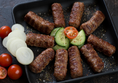 Grilled Cevapi seasoned with herbal spices and served with fresh cucumber, tomatoes and onions.