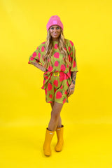 A woman modeling a bright gold and pink strawberry print set with a yellow burnt toast tag on waistband and pink beanie, paired with yellow rain boots, against a solid yellow background