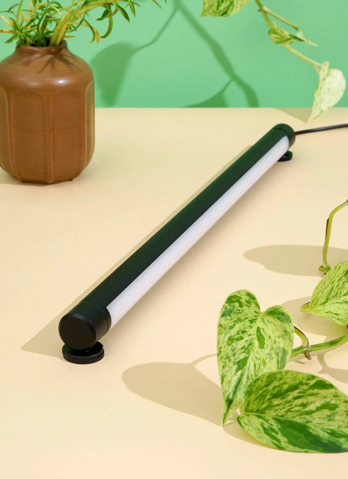 A Black Soltech Grove positioned on a table with a plant in the background, illustrating the product's use for indoor plants.