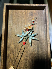 A handmade Chanhua hairpin with bamboo and plum blossom design on a wooden background