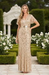 A woman poses in a garden, wearing the R&M Richards 3425 Long Gold Sequin Formal Dress with short sleeves and floral patterns. White roses and greenery provide an elegant backdrop for this stunning evening gown.