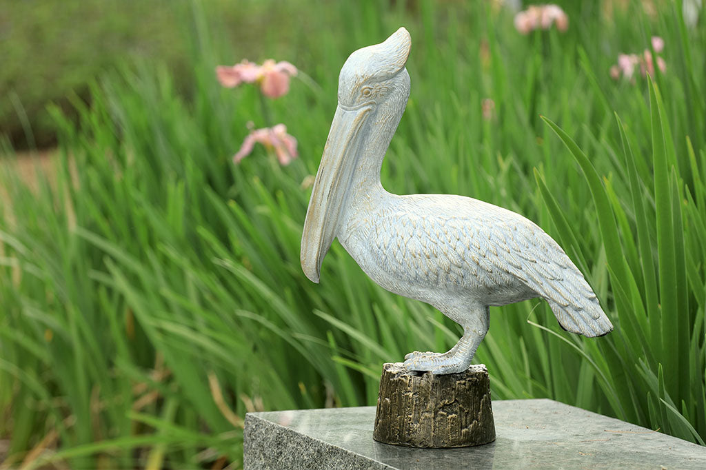 Aluminum garden sculpture of  white pelican standing upon a pier piling.  Shown on marble ledge near iris garden
