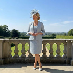 Woman in a plus size Veromia light pastel blue mother of the bride 2 piece suit with a matching fascinator hat standing on a stone ready to attend a wedding.