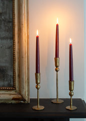 Three lit candles in gold candle holders on a dark surface with a mirror in the background.