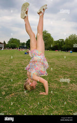 A 5 year old girl in a summer dress does a head stand in the park Stock  Photo