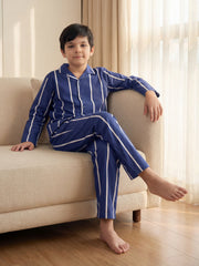 A young boy sits relaxed on a light-colored couch, wearing a blue and white vertical striped pajama set.