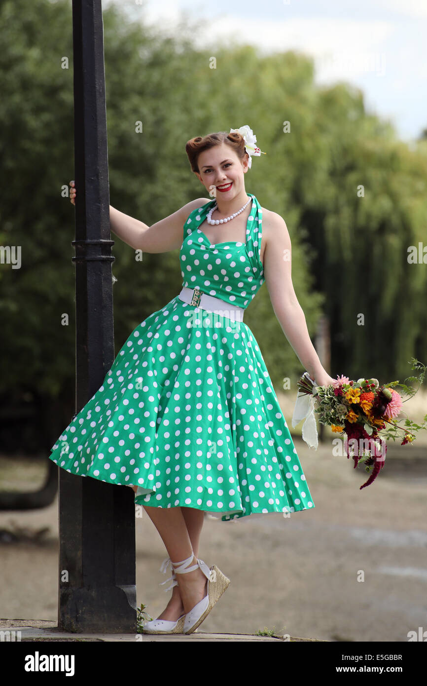 Woman in vintage polka dot dress leaning from a lamp post holding a bunch of flowers Stock Photo